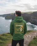 Person wearing a green hoodie with a scenic design, standing on a cliff overlooking the ocean.