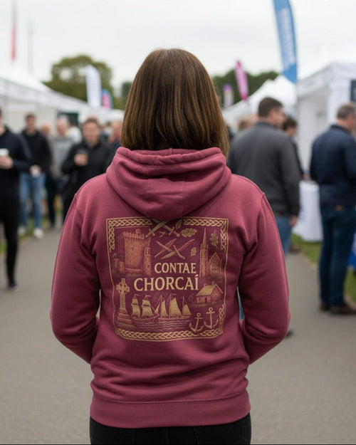 Person wearing a maroon hoodie with gold design and text at an outdoor event.
