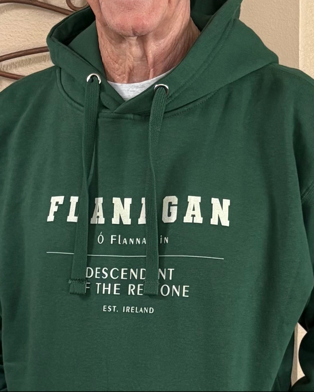 Man wearing a green hoodie with text standing against a decorative wall.